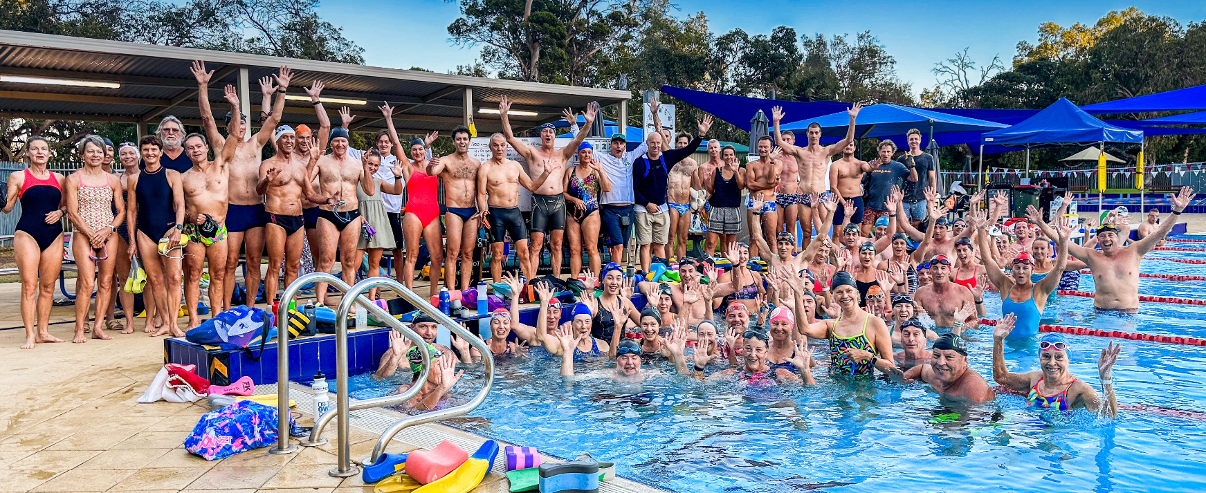 A Swim Smooth squad gathered poolside with hands raised